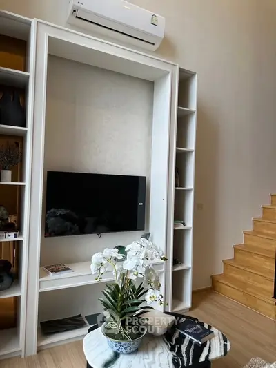 Modern living room with built-in TV unit and air conditioning, featuring elegant decor and wooden staircase.