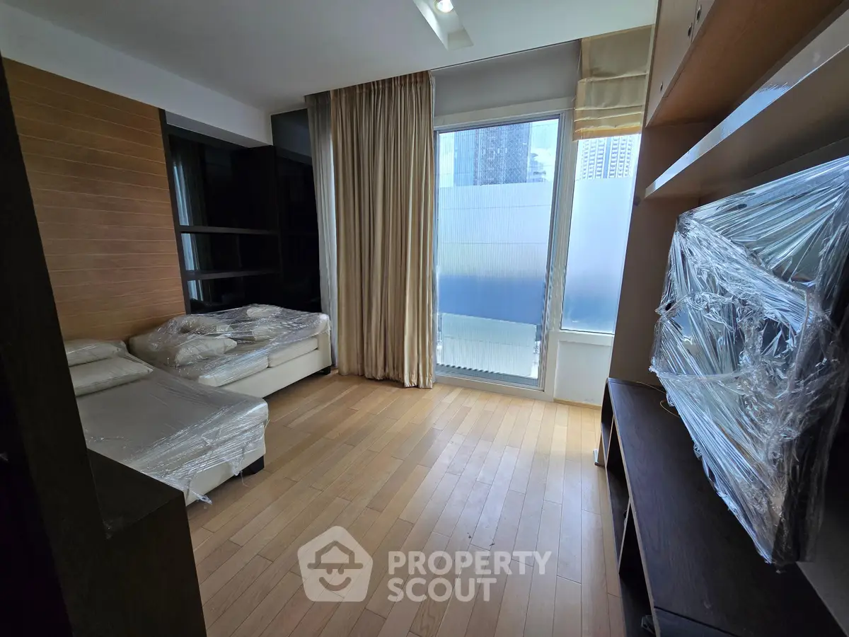 Spacious living room with large window and modern furnishings in a high-rise apartment.