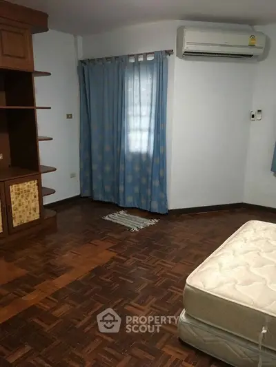 Spacious bedroom with parquet flooring and air conditioning, featuring built-in wooden shelves and blue curtains.