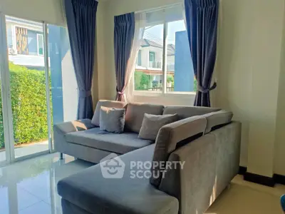 Bright living room with modern gray sofa and large windows overlooking greenery.