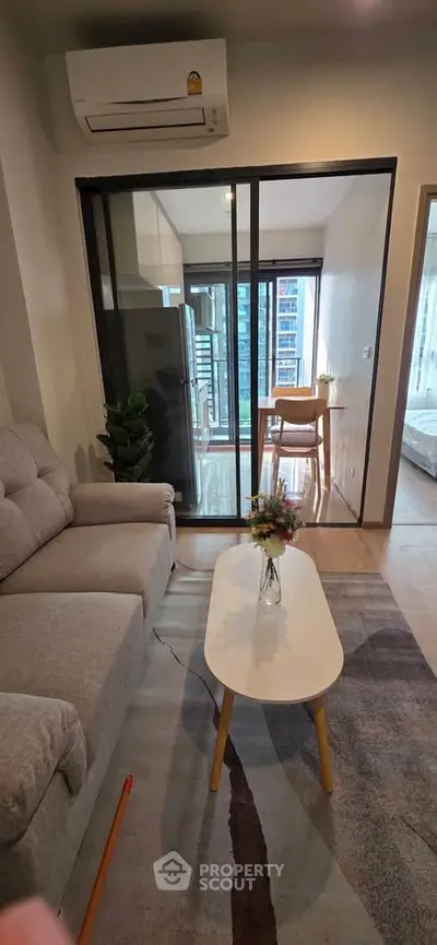 Modern living room with cozy sofa and glass partition leading to dining area with city view.