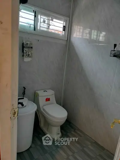 Compact bathroom with modern toilet and tiled walls, featuring a small window for natural light.