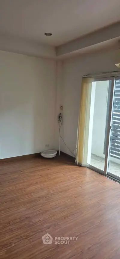 Spacious empty room with wooden flooring and sliding glass door to balcony.