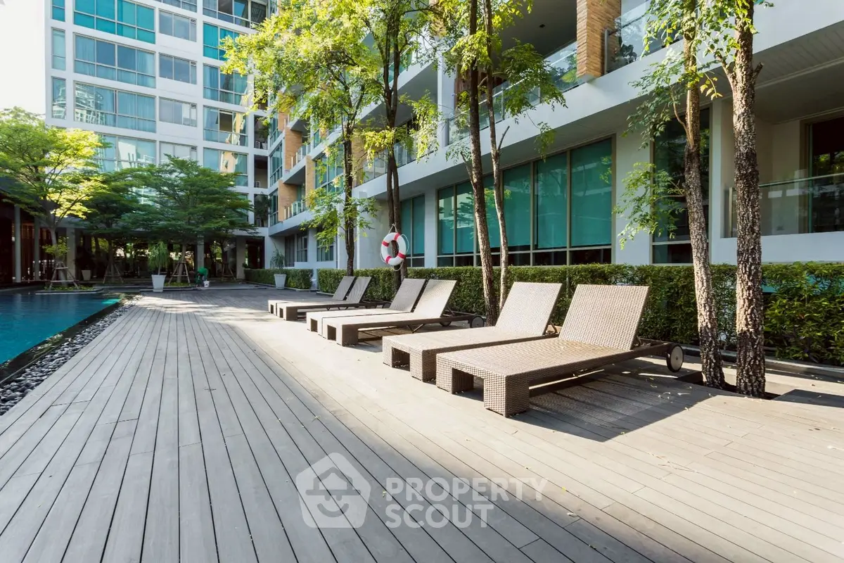 Luxurious condo poolside with modern lounge chairs and lush greenery, perfect for relaxation and leisure.