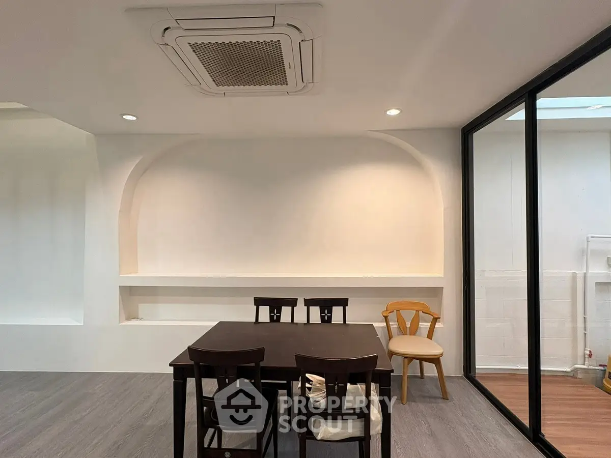 Modern dining area with sleek table and chairs, featuring a minimalist design and large glass window.