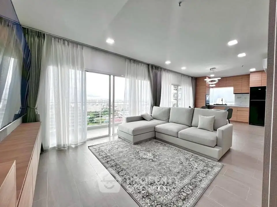 Spacious modern living room with large windows and open kitchen layout, offering a stunning city view.