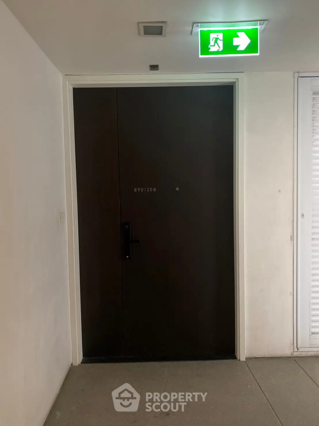 Modern apartment entrance with sleek dark door and emergency exit sign above.