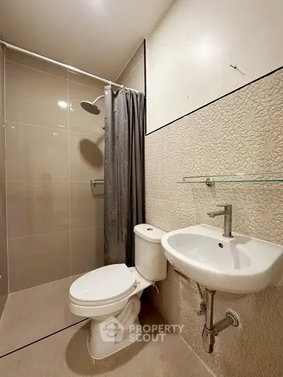 Modern bathroom with sleek fixtures and neutral tiles, featuring a shower and compact sink.