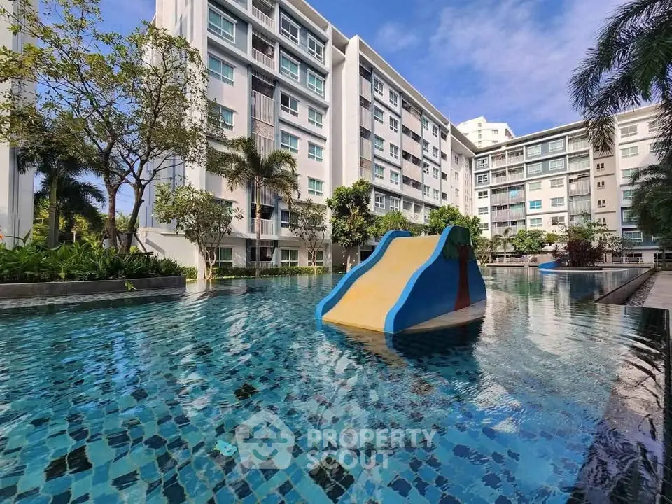 Luxurious apartment complex with stunning pool and slide, surrounded by lush greenery.