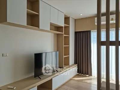 Modern living room with built-in shelves and large TV, featuring natural light and elegant curtains.