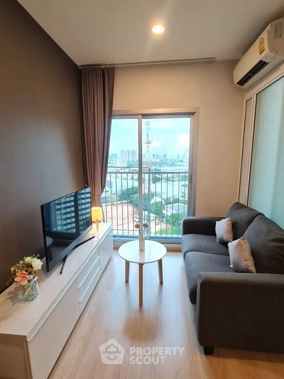 Modern living room with city view, cozy sofa, and sleek TV setup in a high-rise apartment.
