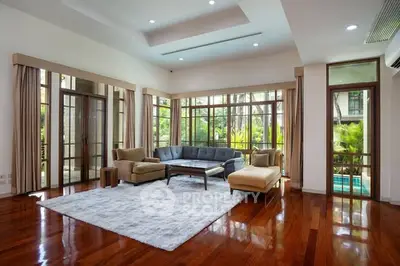 Spacious living room with elegant wooden flooring and large windows offering lush garden views.