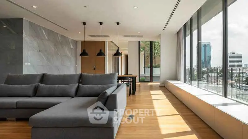 Spacious modern living room with large windows and city view, featuring sleek furniture and elegant lighting.