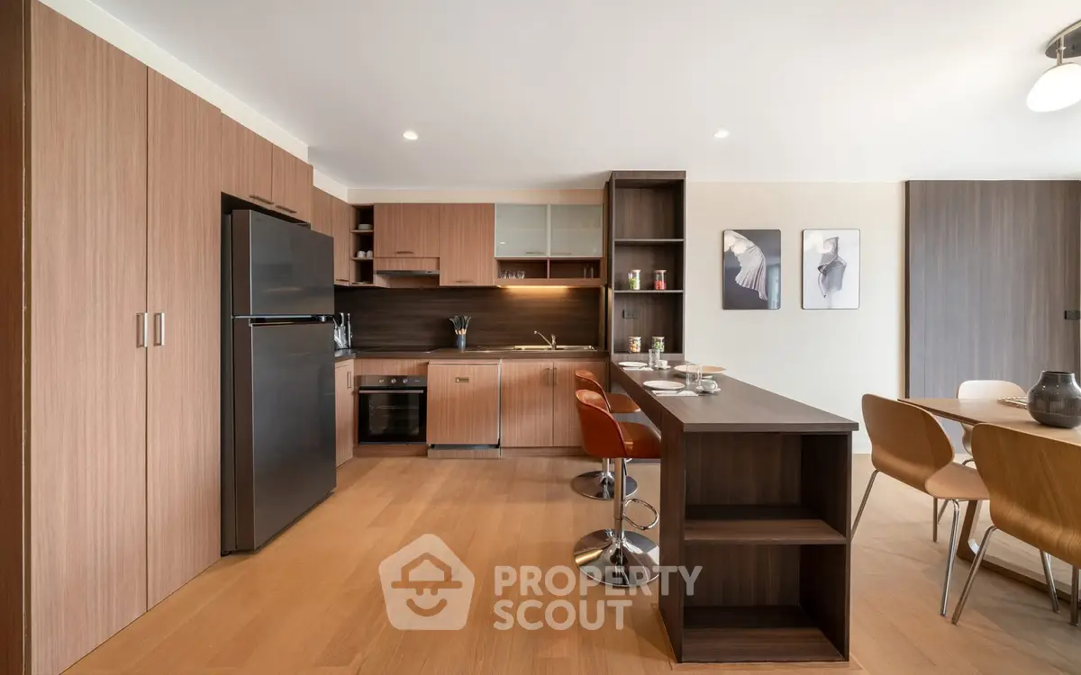 Modern kitchen with sleek wooden cabinetry and open layout, featuring a dining area and stylish decor.