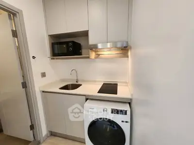 Modern compact kitchen with washing machine and microwave in sleek apartment.