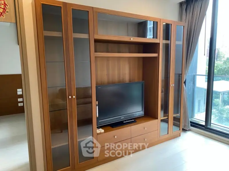 Spacious living room with elegant wooden entertainment center and large window view.