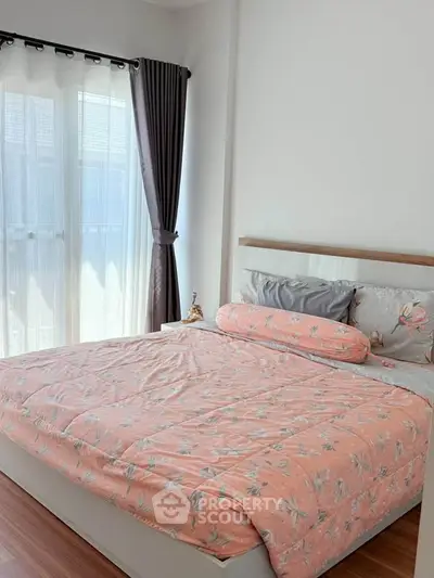 Cozy bedroom with large window and stylish curtains, featuring a comfortable bed with floral bedding.