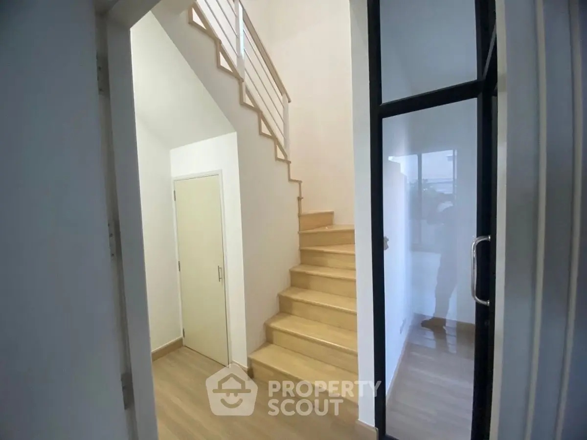 Modern interior with wooden staircase and glass door, showcasing minimalist design.