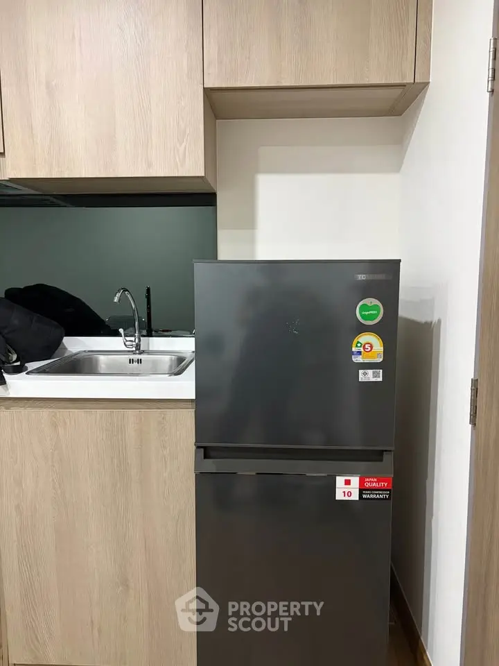 Modern kitchen with sleek fridge and wooden cabinetry in compact apartment