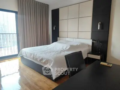 Modern bedroom with large window and stylish decor in urban apartment.