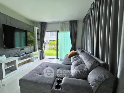 Modern living room with plush gray sofa and large TV, overlooking a lush garden.