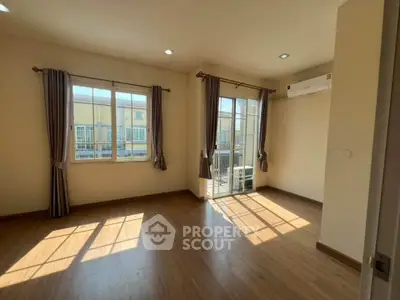 Spacious sunlit room with wooden flooring and large windows in modern apartment.