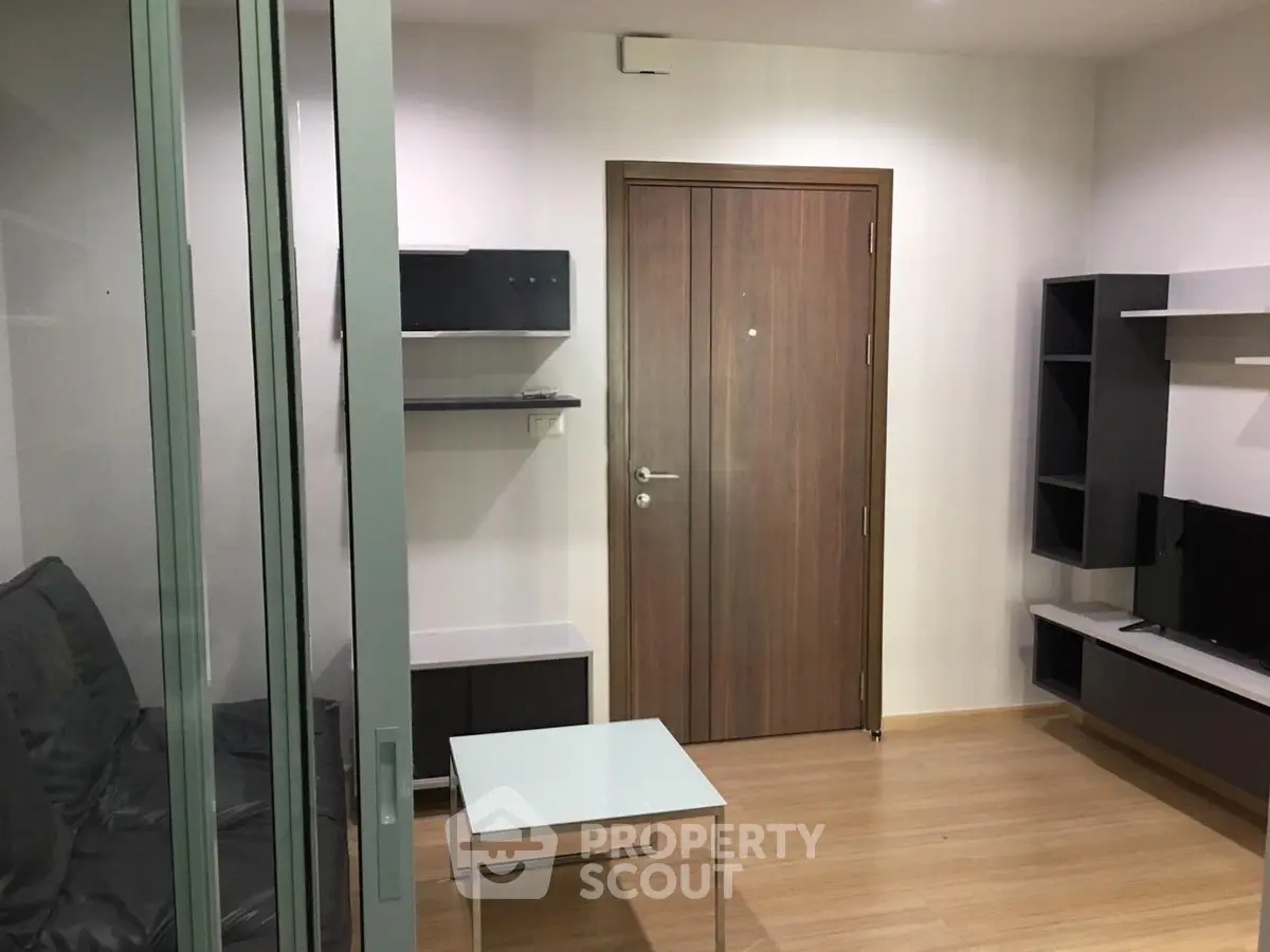 Modern living room with sleek furniture and wooden flooring, featuring a glass sliding door and stylish shelving.