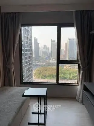 Modern bedroom with city view through large window in high-rise apartment.