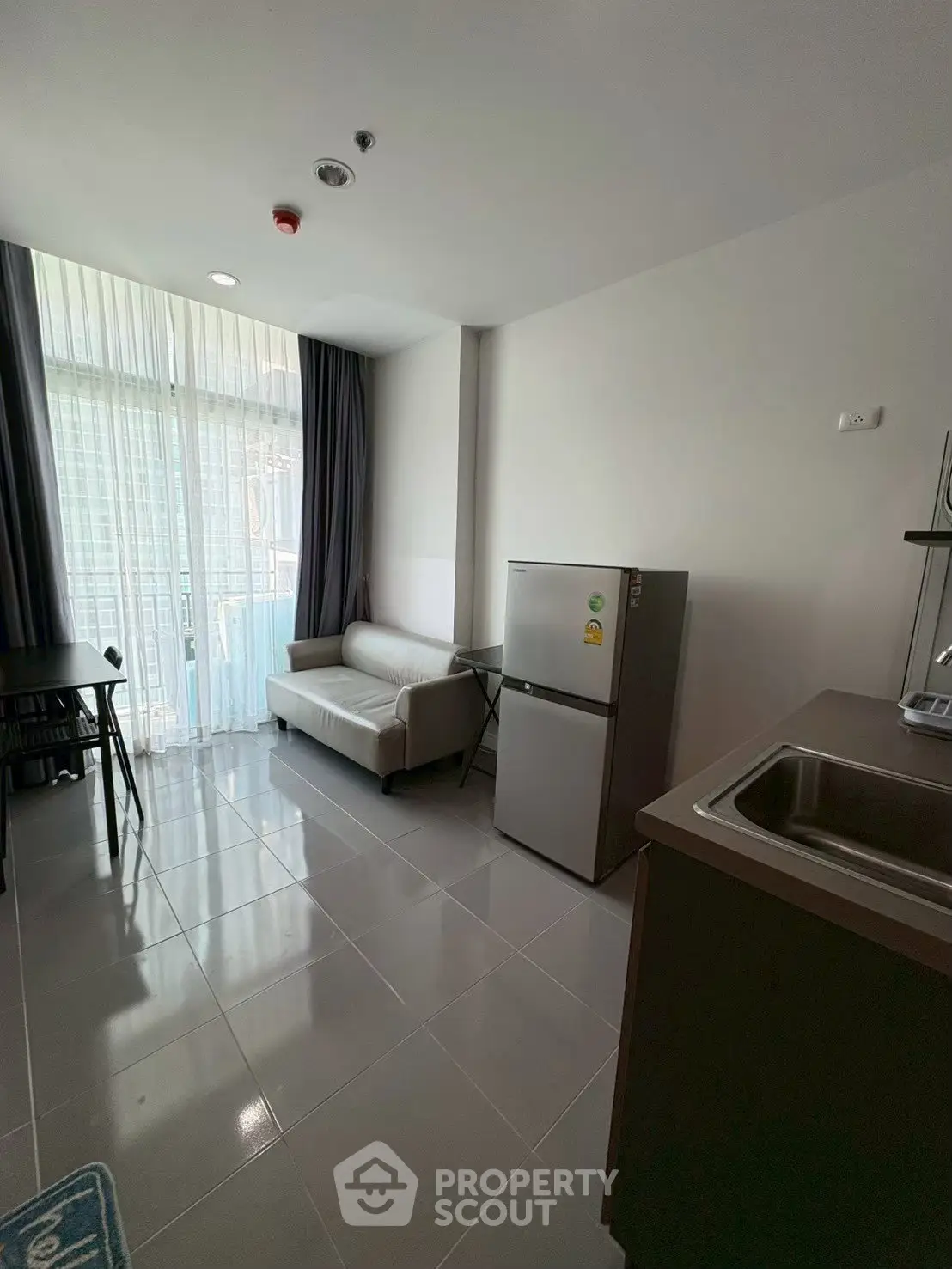 Modern living room with sleek furniture and natural light, featuring a compact kitchen and balcony access.