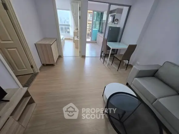 Modern living room with wooden flooring and stylish furniture, leading to a bright balcony area.