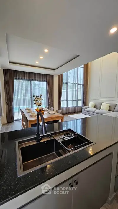 Luxurious open-plan living room with modern kitchen and elegant dining area, featuring floor-to-ceiling windows.