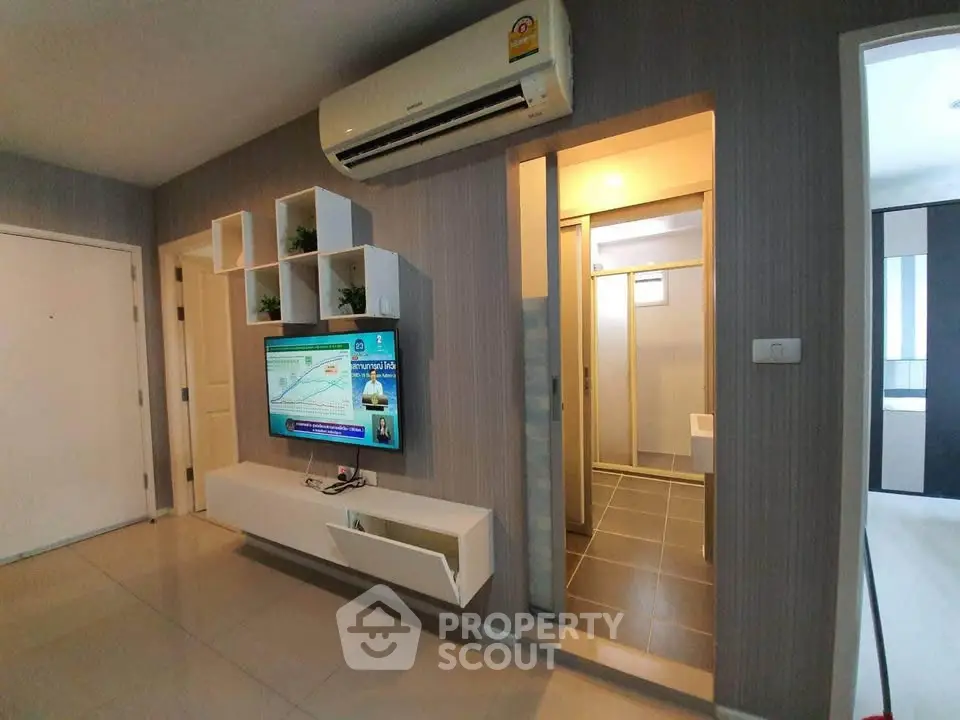 Modern living room with wall-mounted TV and air conditioning, adjacent to a sleek bathroom entrance.