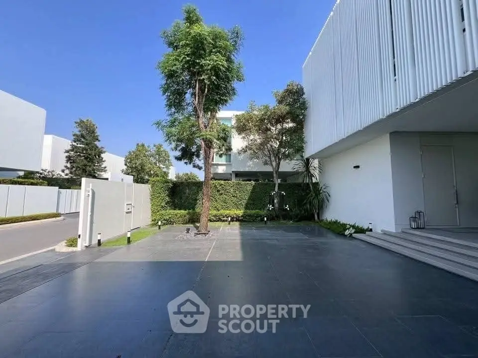 Modern minimalist home exterior with spacious driveway and lush greenery