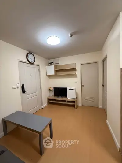 Cozy living room with modern decor and wooden flooring, featuring a wall-mounted clock and minimalist furniture.