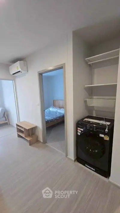 Modern apartment interior with bedroom and laundry area featuring a washing machine and shelving.