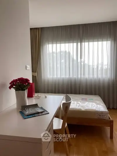 Bright bedroom with large window, wooden flooring, and modern furniture, perfect for a cozy living space.