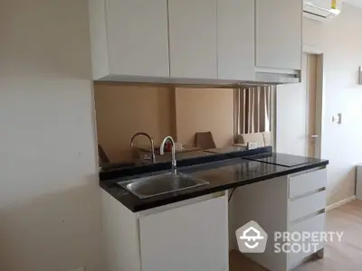 Modern kitchen with sleek white cabinetry and black countertop, featuring a built-in sink and ample storage space, perfect for culinary enthusiasts.