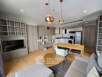 Modern living room with stylish furniture and open kitchen layout, featuring wooden flooring and contemporary lighting.