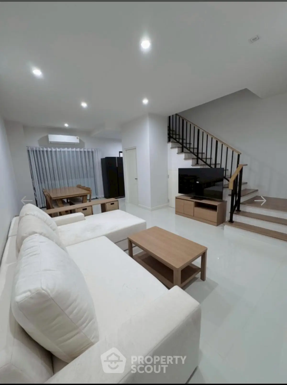 Spacious modern living room with white sofa and wooden furniture, featuring a sleek staircase.