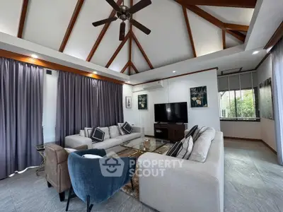 Spacious living room with high ceiling and modern decor, featuring a cozy seating area and large windows.