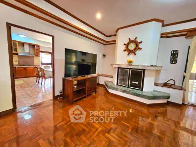 Charming living room with fireplace and wooden flooring, open view to kitchen area.