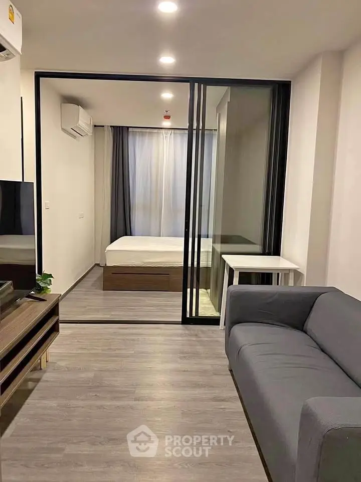 Modern apartment interior with cozy living room and bedroom separated by glass sliding doors.