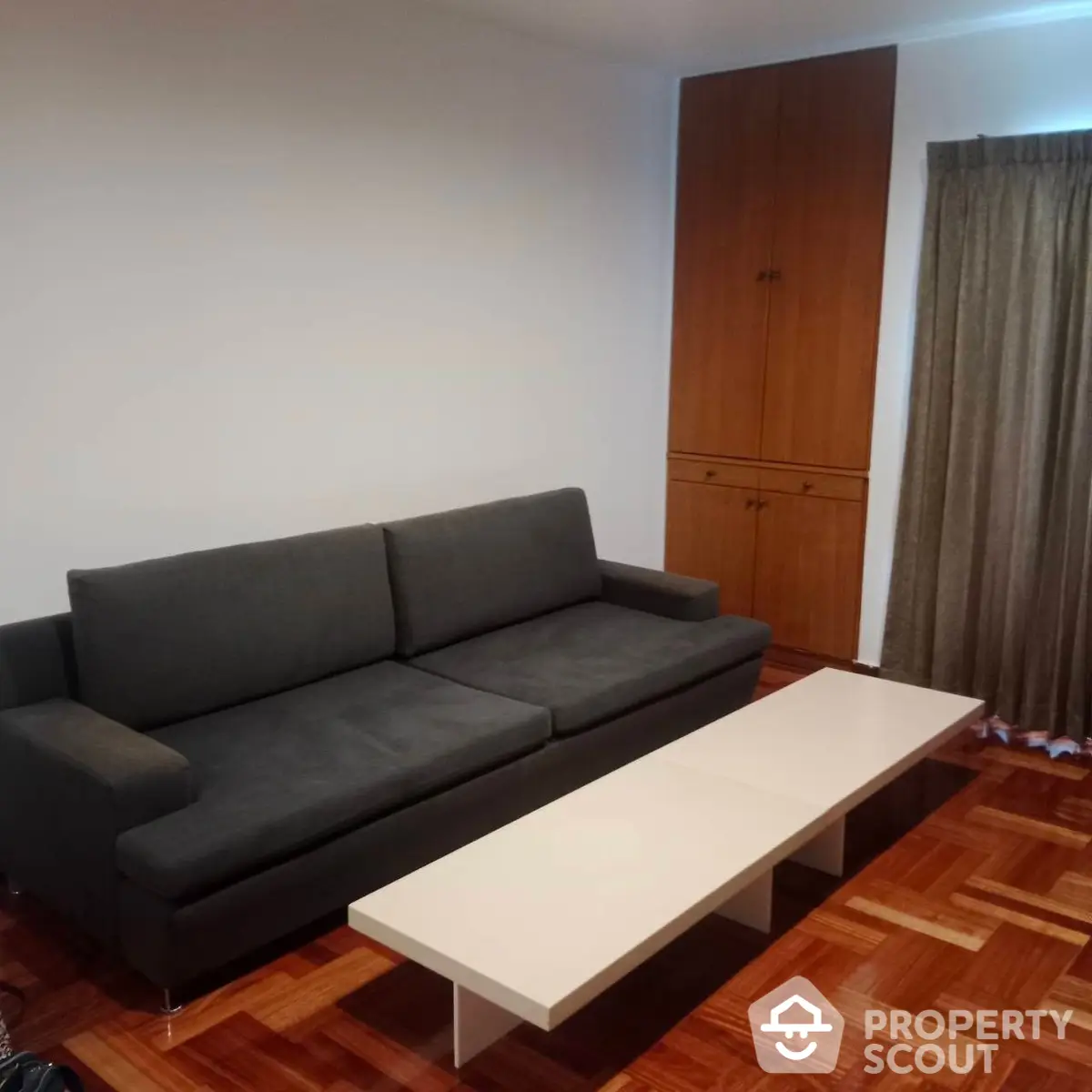 Spacious living room with polished parquet flooring, modern grey sofa, and a sleek white coffee table, complemented by warm-toned wooden cabinetry.