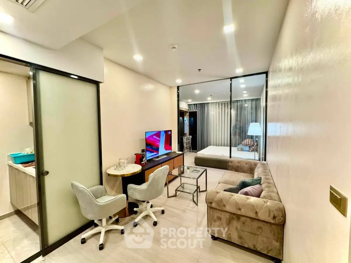Modern living room with glass partition, stylish furniture, and open kitchen layout in a contemporary apartment.