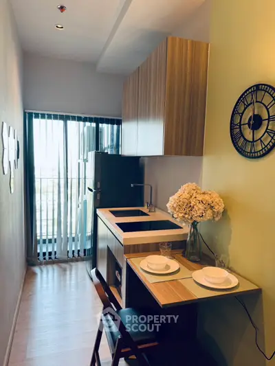 Modern compact kitchen with stylish wooden cabinets and dining area, featuring a sleek design and natural light.