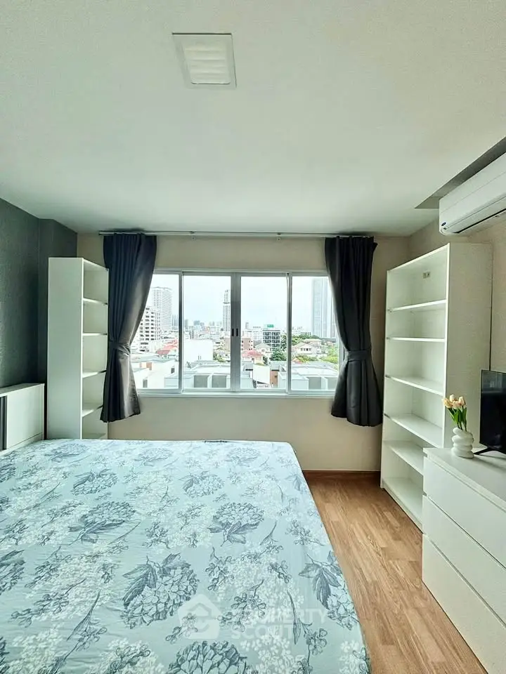 Bright bedroom with large window offering city view, featuring modern furnishings and ample storage space.