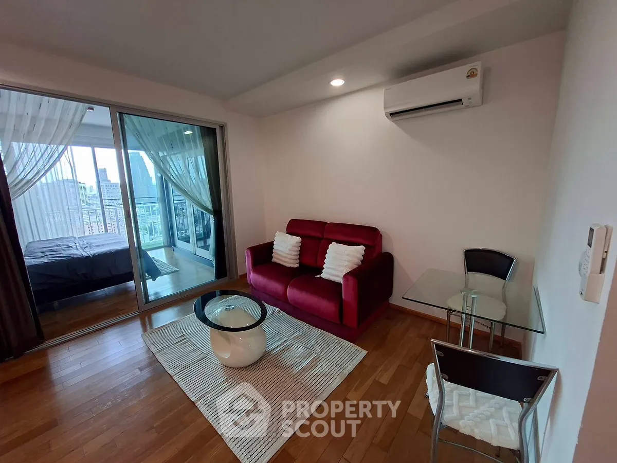 Modern living room with red sofa, glass table, and city view balcony in a stylish apartment.