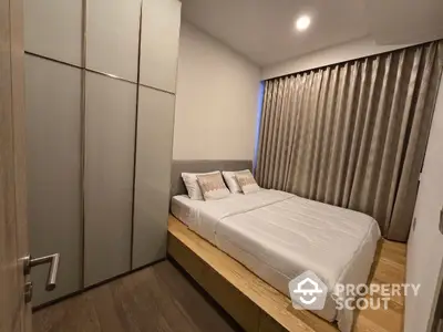 Modern bedroom with sleek built-in wardrobes and a cozy bed, complemented by warm wooden flooring and elegant gray curtains.