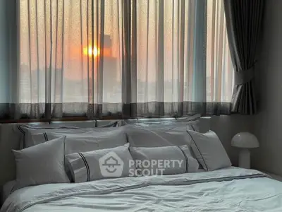 Cozy bedroom with elegant bedding and sunset view through sheer curtains.