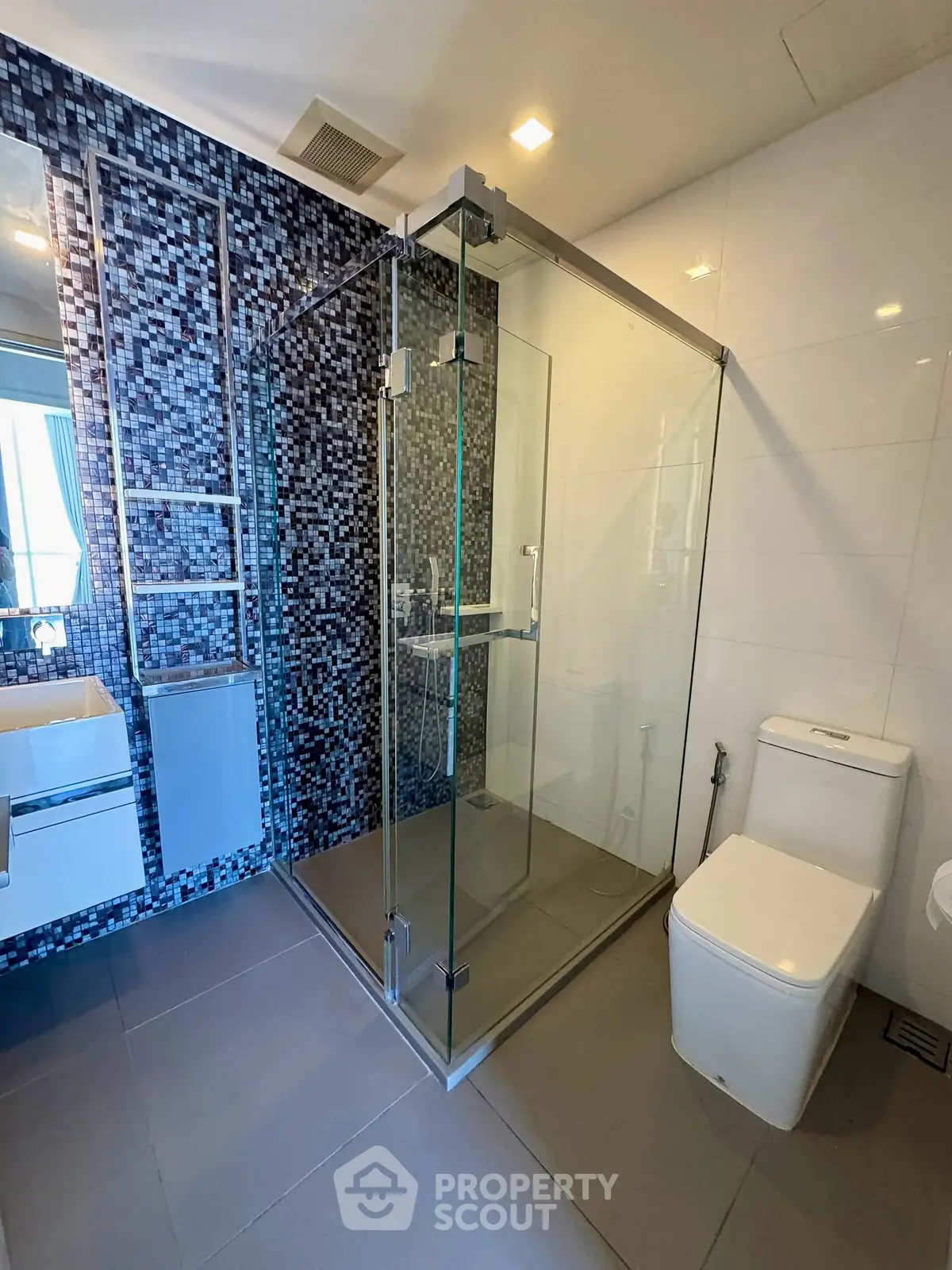 Modern bathroom with glass shower enclosure and mosaic tile accent wall.